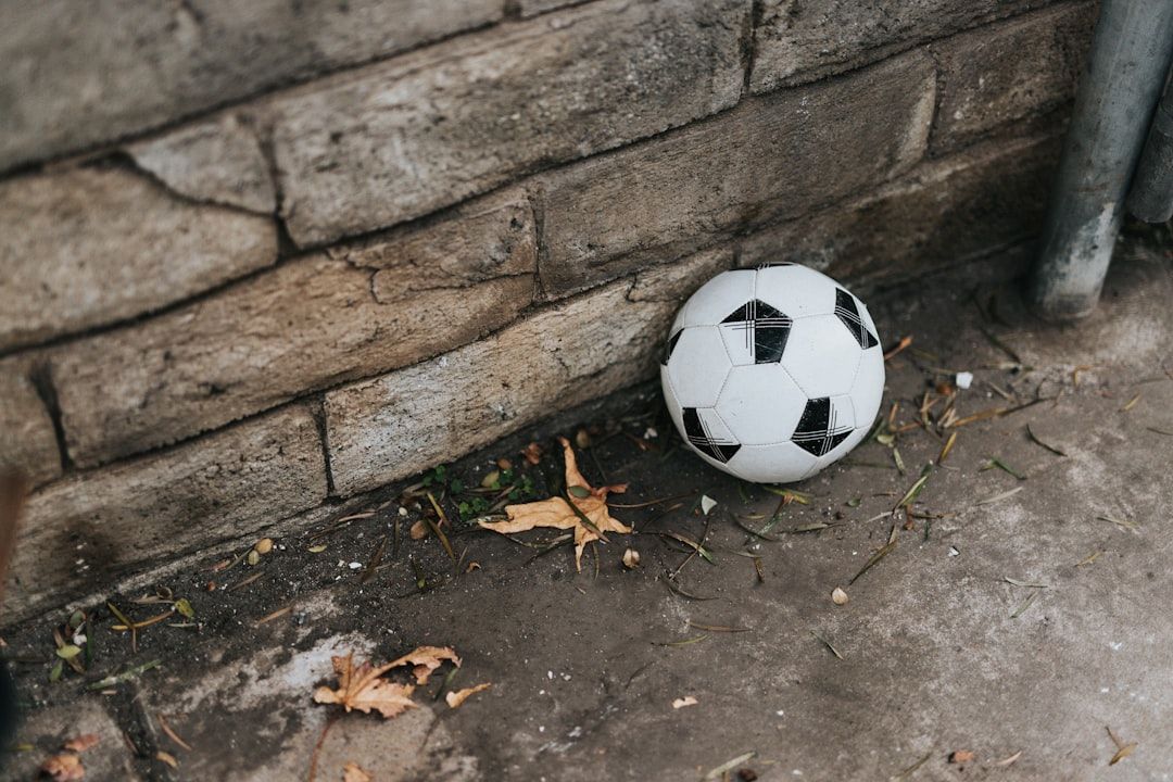 En smutsig fotboll ligger vid en stenvägg med löv på marken.